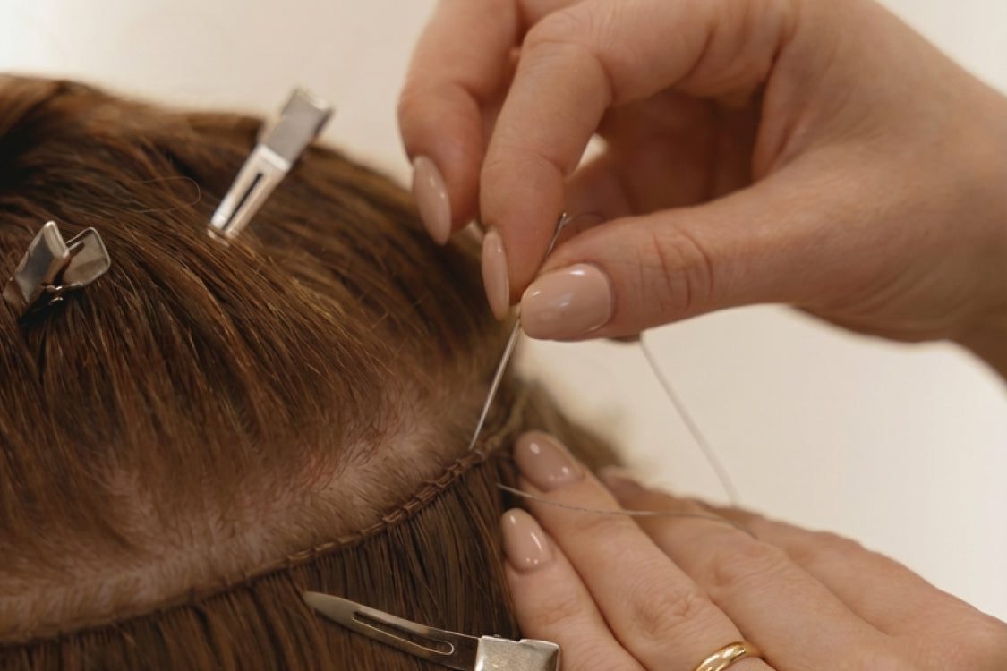 Hands sewing hair extensions into braided natural hair